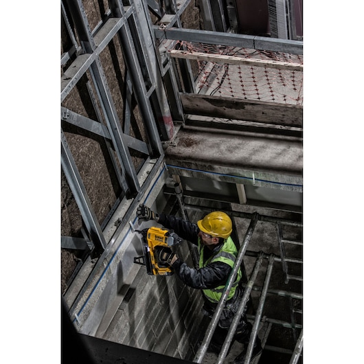 A construction worker wearing a yellow hard hat and high-visibility vest uses a DEWALT DCN890P2 tool to install metal frames
