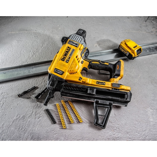 A DEWALT DCN890P2 cordless nail gun is shown on a concrete surface, alongside a battery pack, metal strip, nail cartridges