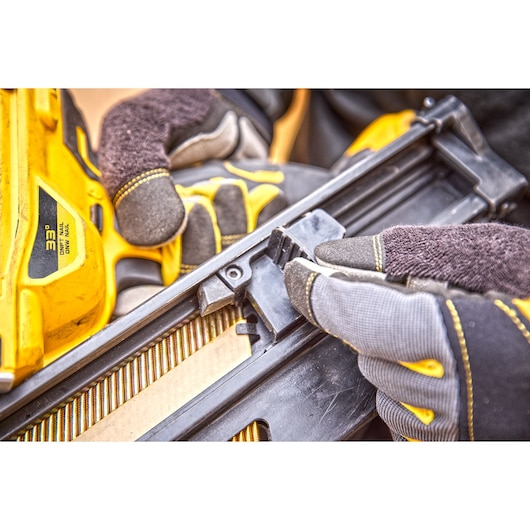 Close-up of gloved hands handling a DEWALT 33° nail gun, adjusting or loading nails into the magazine.