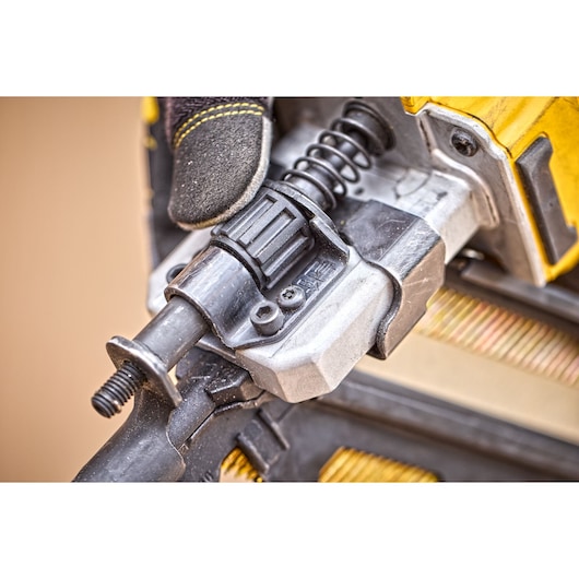 Close-up of a DEWALT DCN930N power tool component, focusing on the metal and plastic mechanism with a visible spring, and a gloved hand adjusting the part.