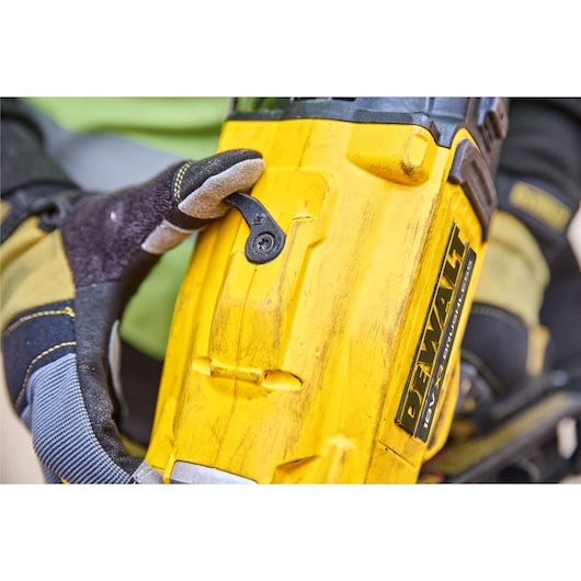Close-up of a person wearing work gloves operating a yellow DEWALT power tool, likely a cordless nailer.
