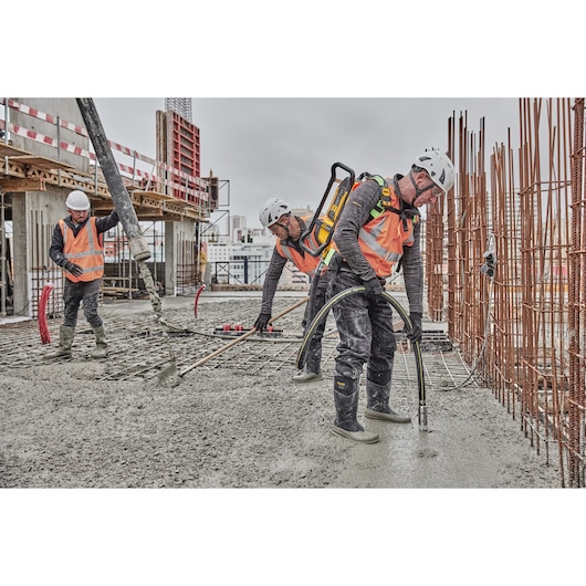 Construction workers wearing safety gear and high-visibility vests are working on a concrete slab. One worker uses a DEWALT