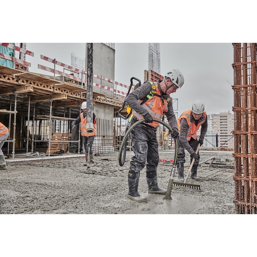 Construction workers wearing safety helmets, gloves, and orange vests are working on a building site. They are leveling