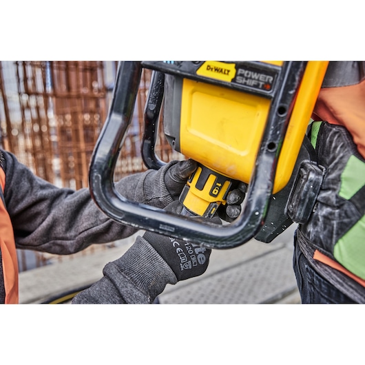 Close-up of a person wearing gloves and safety clothing operating a DEWALT Power Shift tool at a construction site.