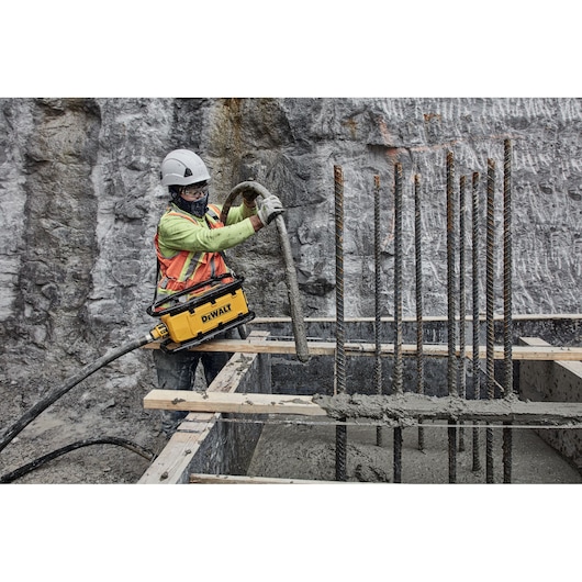A construction worker wearing safety gear operates a DEWALT DCPS320N power tool at a building site, using it to work with