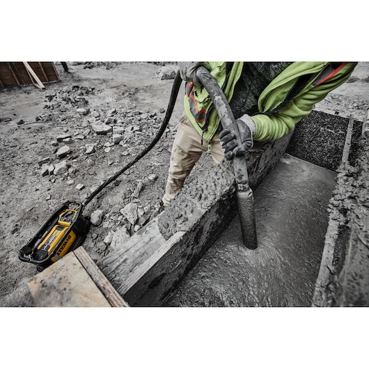 A person wearing work gloves and a safety vest uses a DEWALT concrete vibrator on a construction site to smooth and compact
