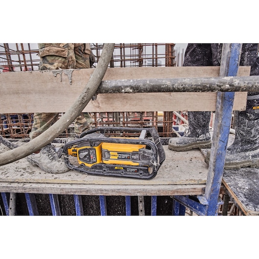 A DEWALT DCPS320N power tool placed on a construction site platform, surrounded by workers' legs and construction materials