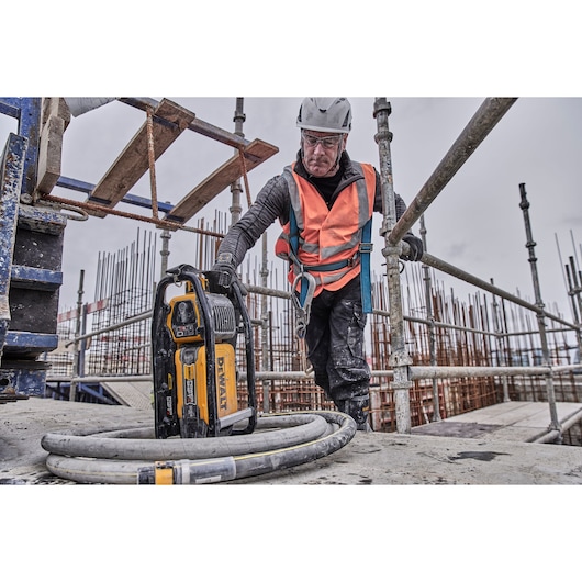 A DEWALT DCPS320N portable device is placed on a construction site platform. A worker wearing a helmet, gloves, and an