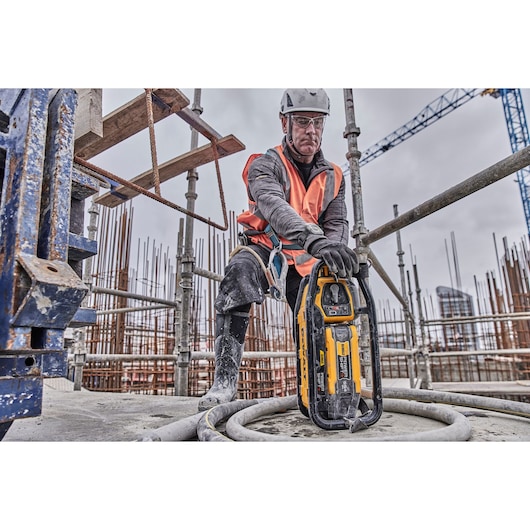 A construction worker wearing safety gear and an orange vest is using a DEWALT DCPS320N power tool at a building site