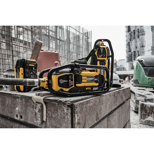 DEWALT Power Shift chainsaw and battery on a construction site with buildings and equipment in the background.