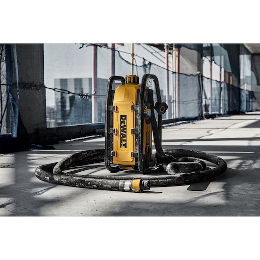DEWALT tool with hose on construction site floor, surrounded by safety netting and scaffolding in sunlight.