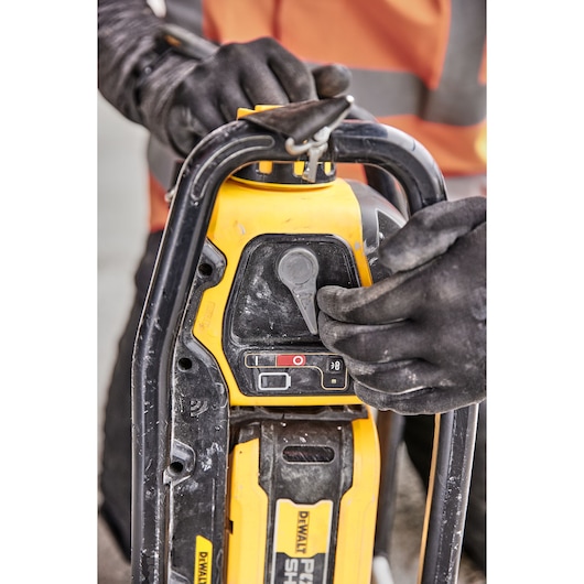 Closeup of gloved hands operating a yellow DEWALT power tool with visible controls and sturdy handle.