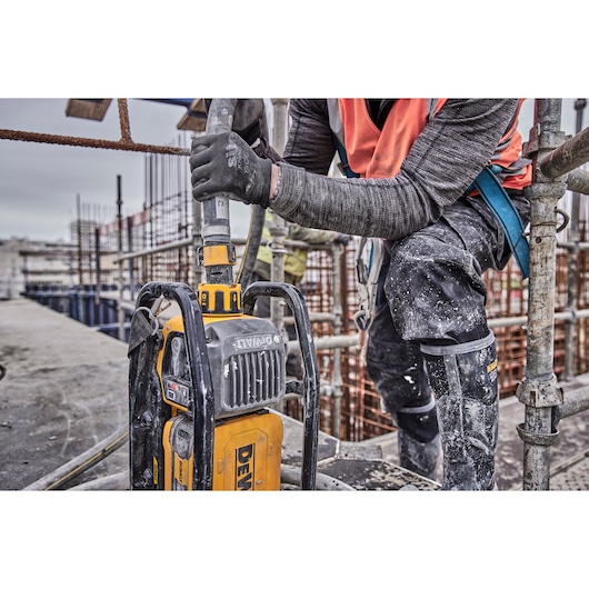 Worker using a DEWALT power tool at a construction site, wearing safety gear and gloves.