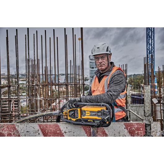 DEWALT DCPS320N saw held by a worker in safety gear at a construction site with metal rebar in the background.