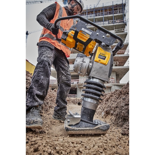 A construction worker wearing an orange safety vest and helmet operates a DEWALT DCPS660N power tool, specifically a