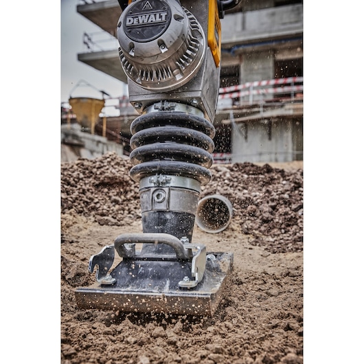 Close-up view of a DEWALT-branded compactor machine actively compressing soil at a construction site, with dirt particles