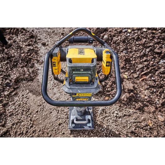 DEWALT cordless compactor with yellow body shown on rough soil, viewed from above.