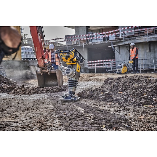 DEWALT compactor in use on a construction site with workers and heavy machinery visible in the background.