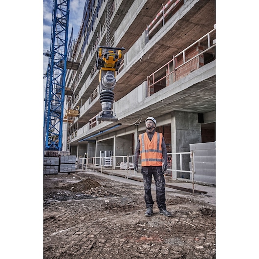 DEWALT power tool in use at a construction site with a worker in a high-visibility vest in the foreground.