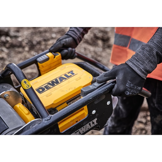 Person wearing gloves operates DEWALT outdoor power equipment on a worksite.