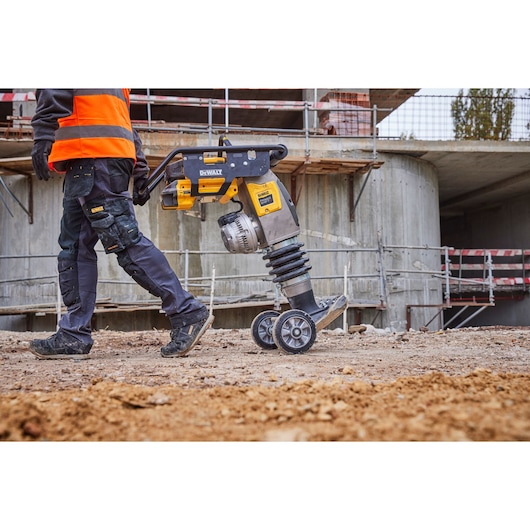 DEWALT cordless demolition hammer on wheels being moved at a construction site by a worker in safety gear.