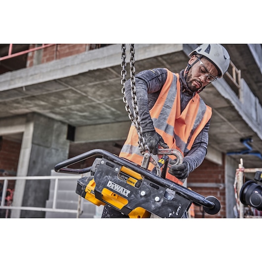 Worker lifts DEWALT DCPS660N tool with safety gear at construction site. Concrete structure visible in background.