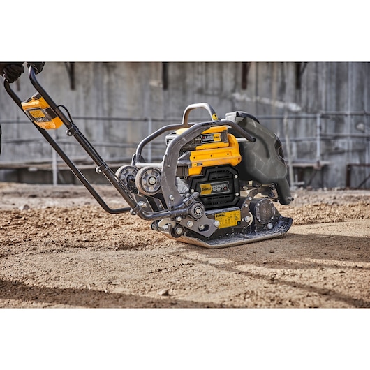 A DEWALT plate compactor, model DCPS7154N, shown on a construction site, being used to compact soil. The machine features a