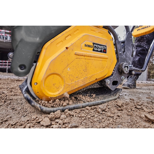 Close-up view of a DEWALT Power Shift plate compactor operating on dirt at a construction site.