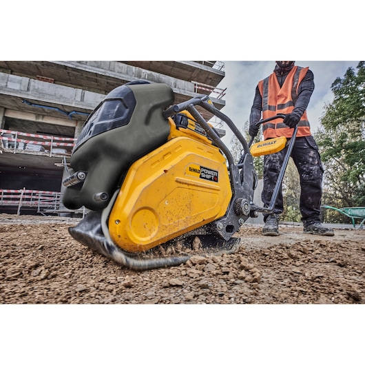 A DEWALT Power Shift plate compactor being operated on a construction site, compacting soil with a worker in a safety vest