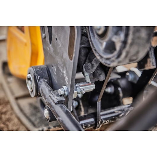 Close-up of a gloved hand adjusting a metal component on a DEWALT tool with bolts and mechanical parts visible.