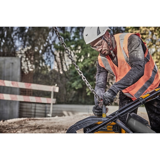 Worker in hi-vis vest and helmet operates DEWALT tool and chain at an outdoor construction site.