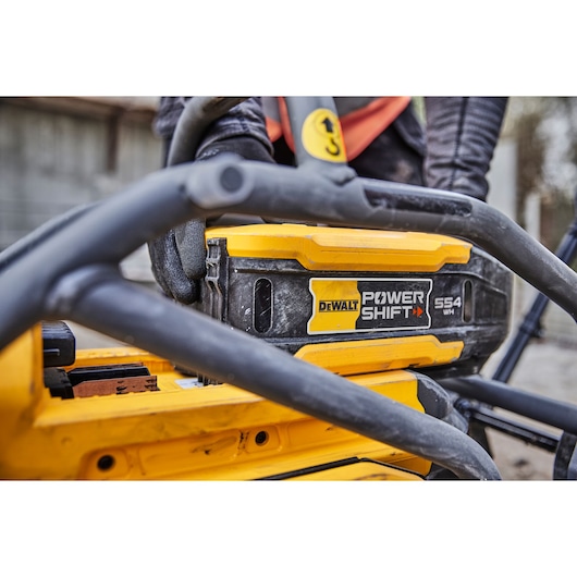 Close-up of a DEWALT Power Shift 554 WH battery in a yellow tool, with worker's gloved hand visible.