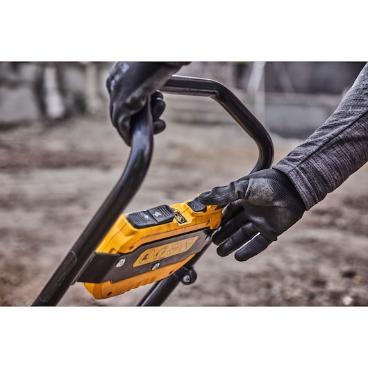 Gloved hands operating a yellow DEWALT tool control panel outdoors with a black metal handle.