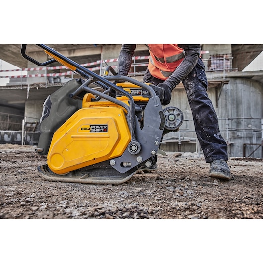 DEWALT plate compactor DCPS7154N used by worker on a construction site with soil and concrete structures.