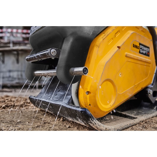 Close-up of a DEWALT tool spraying water onto the ground, showing machine details and yellow casing.