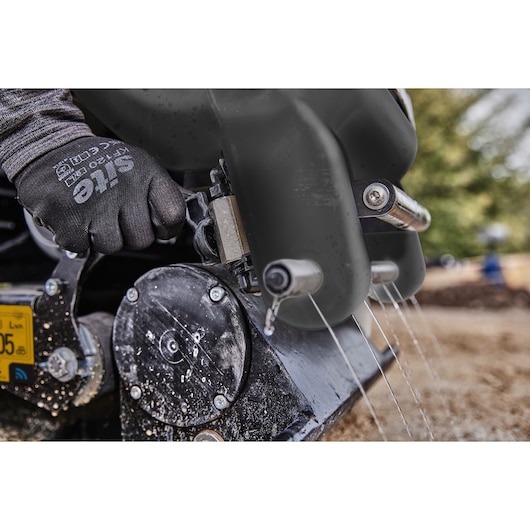Close-up of a gloved hand operating a wet power tool outdoors, water spraying from metal nozzles.