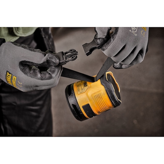 Close-up of gloved hands connecting a strap to a yellow DEWALT portable device, likely a radio or speaker.