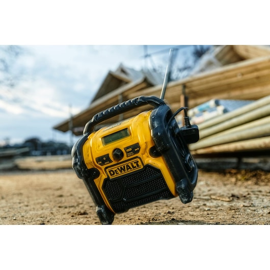 A yellow and black DEWALT portable radio, model DCR020, is placed on a construction site with wooden beams and structures in