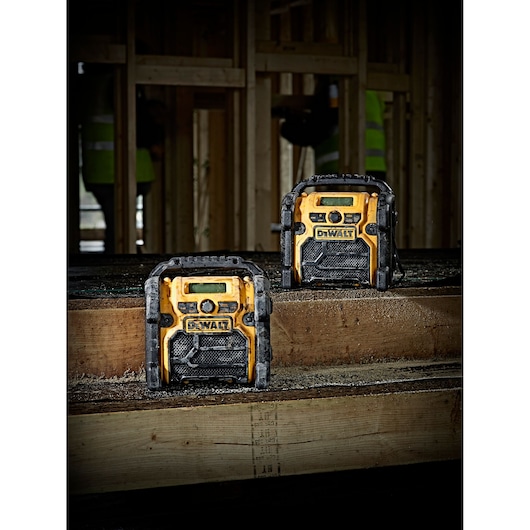 Two DEWALT portable radios placed on wooden beams at a construction site with unfinished wooden framing in the background.