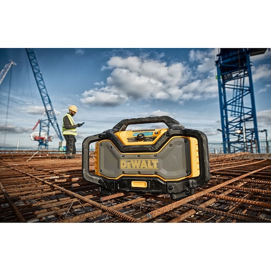 DEWALT jobsite radio on rebar at a construction site with cranes and worker in safety gear in the background.