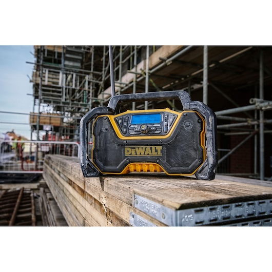 DEWALT jobsite radio on wooden planks at a construction site, surrounded by scaffolding and building materials.