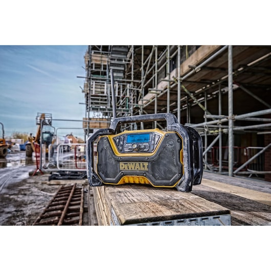 DEWALT portable radio sits on wooden planks at a construction site, surrounded by scaffolding and equipment.