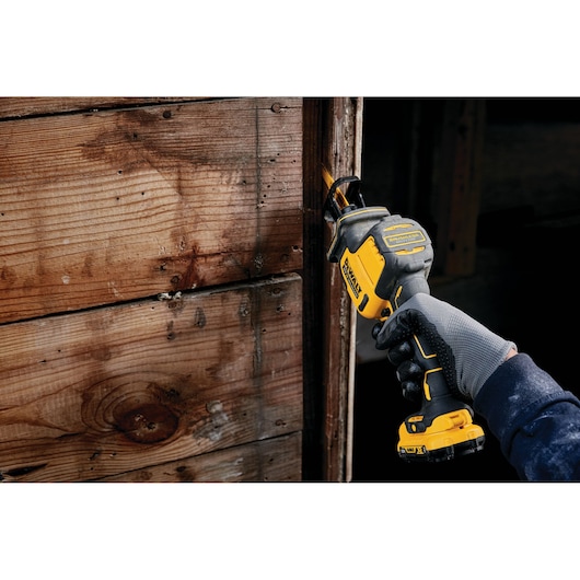 Gloved hand cutting wood with a DEWALT cordless reciprocating saw, model DCS312NT.