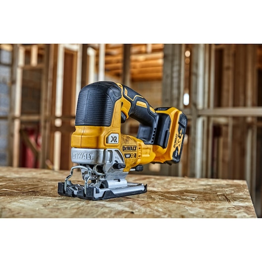 A yellow and black DEWALT cordless jigsaw (model DCS334N) placed on a wooden surface in a construction site setting.