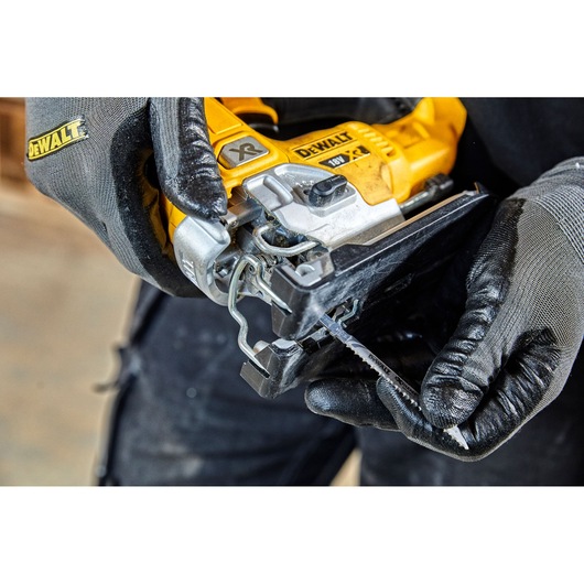 Close-up of a person wearing gloves handling a DEWALT 18V XR cordless jigsaw, preparing to insert or remove the saw blade.