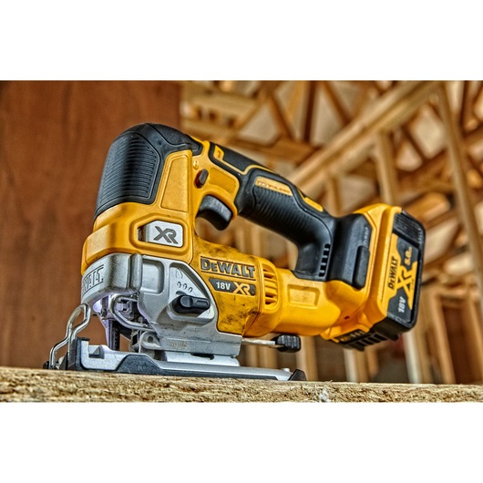 A close-up of a DEWALT 18V XR cordless jigsaw placed on a wooden surface at a construction site.