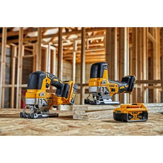 Two DEWALT cordless jigsaws and a DEWALT 18V XR battery are shown on a wooden surface, with a timber construction frame in the background.