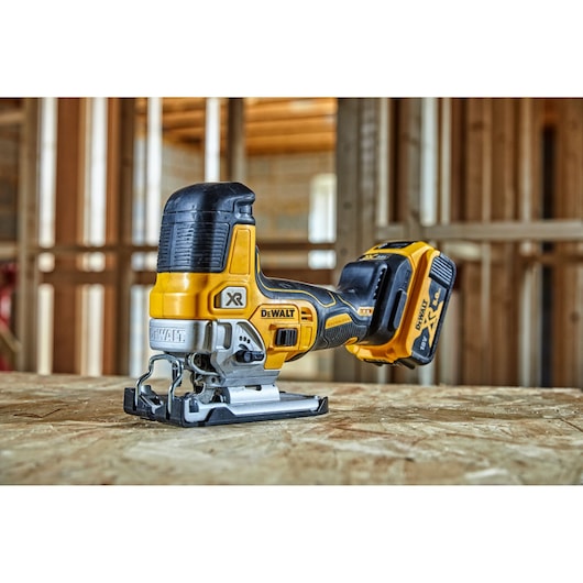 A DEWALT cordless jigsaw, model DCS335P2, placed on a wooden surface in an unfinished indoor construction site.