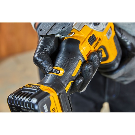 Close-up of a person wearing black gloves holding a DEWALT DCS335P2 cordless power tool, showing the handle, battery, and controls.