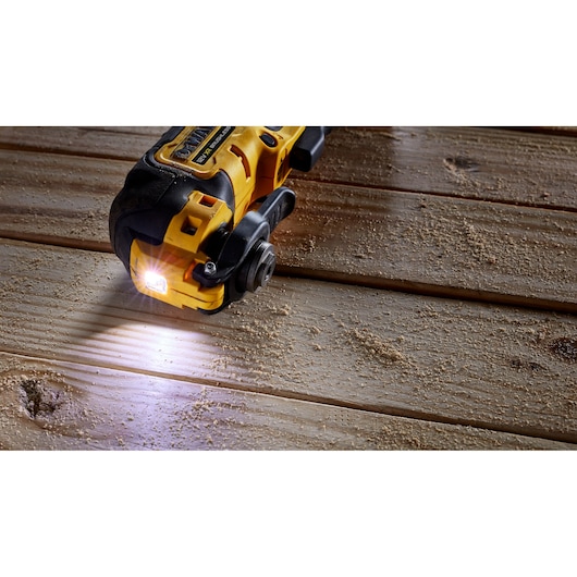 DEWALT power tool with light cutting wood, creating sawdust on wooden surface.